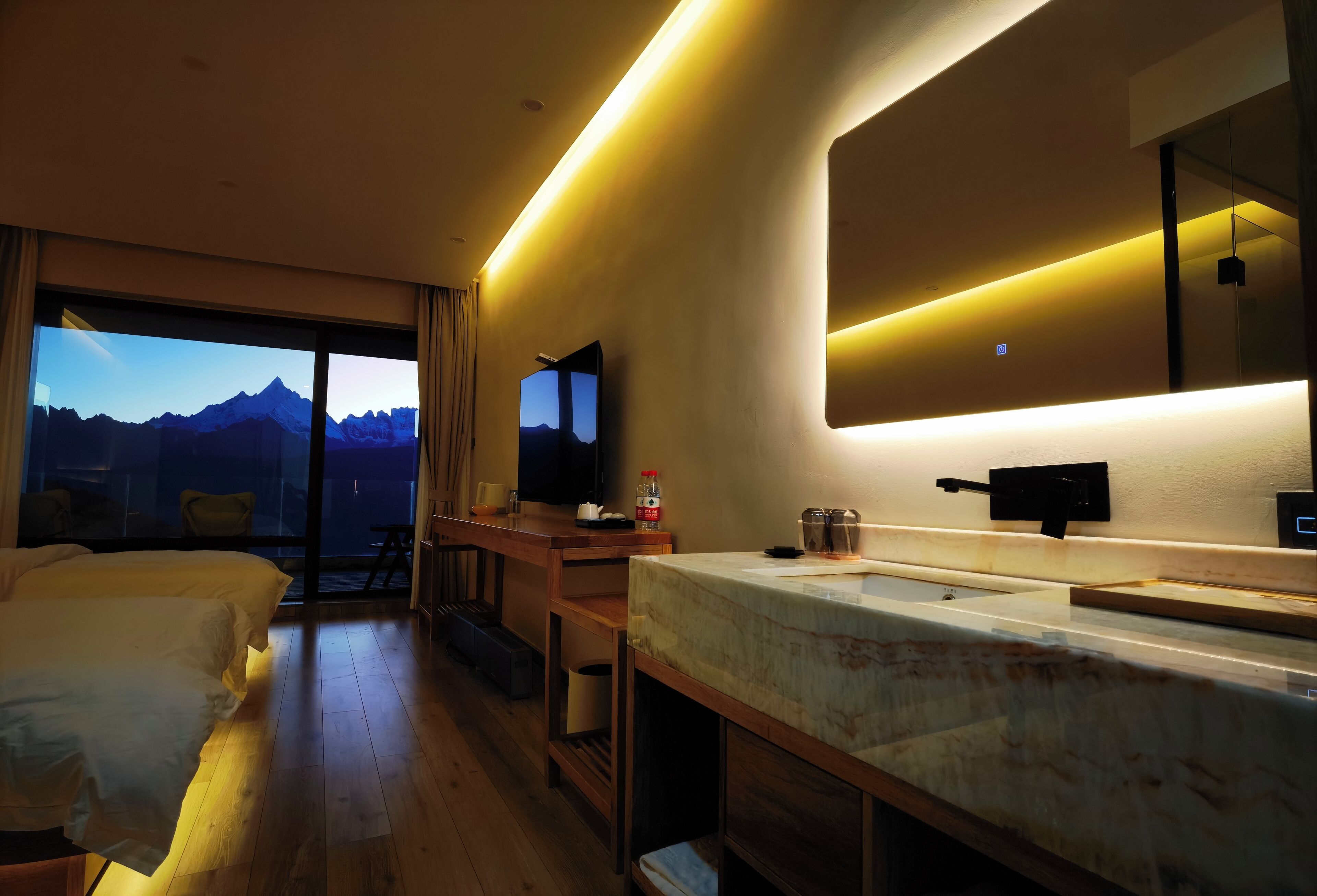 Habitació d'hotel moderna amb un llit gran, escriptori, bany amb un mirall gran i vista a les muntanyes per la finestra.