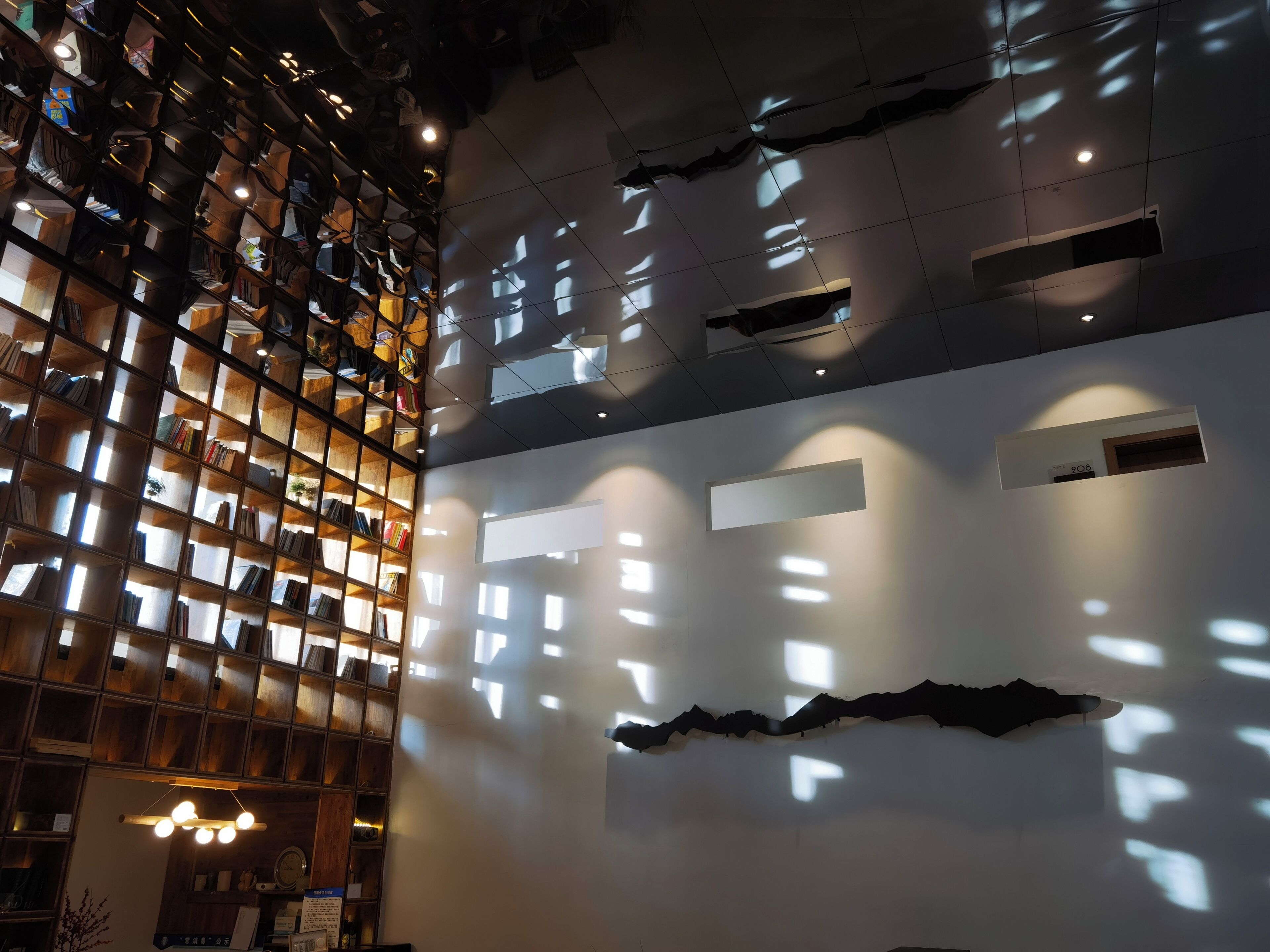 Un interior moderno con una amplia estantería abierta llena de libros, un diseño de pared minimalista con recortes geométricos e iluminación empotrada en el techo.