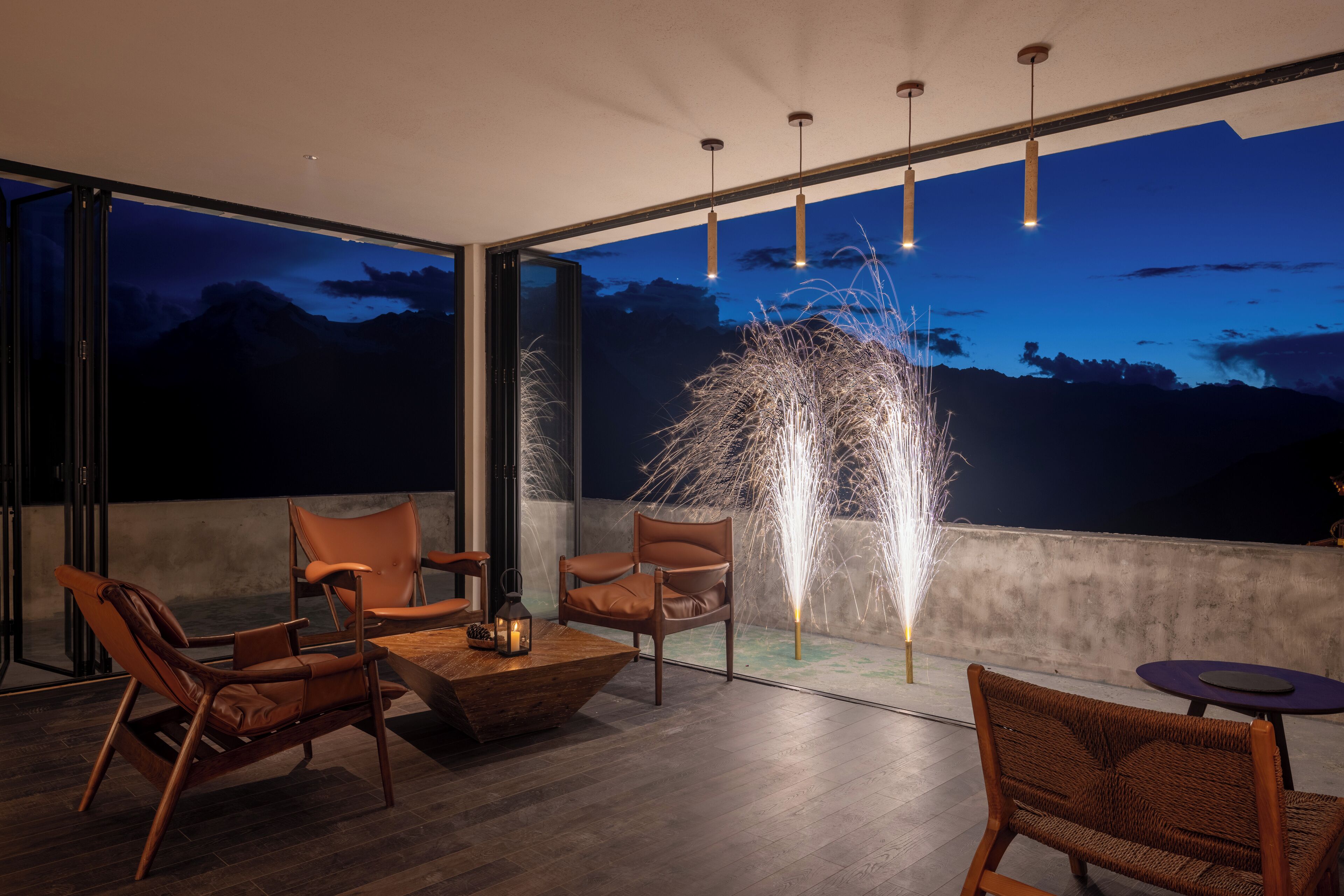 A modern outdoor seating area with leather chairs and a wooden table, large windows with a night sky view, and decorative lighting.