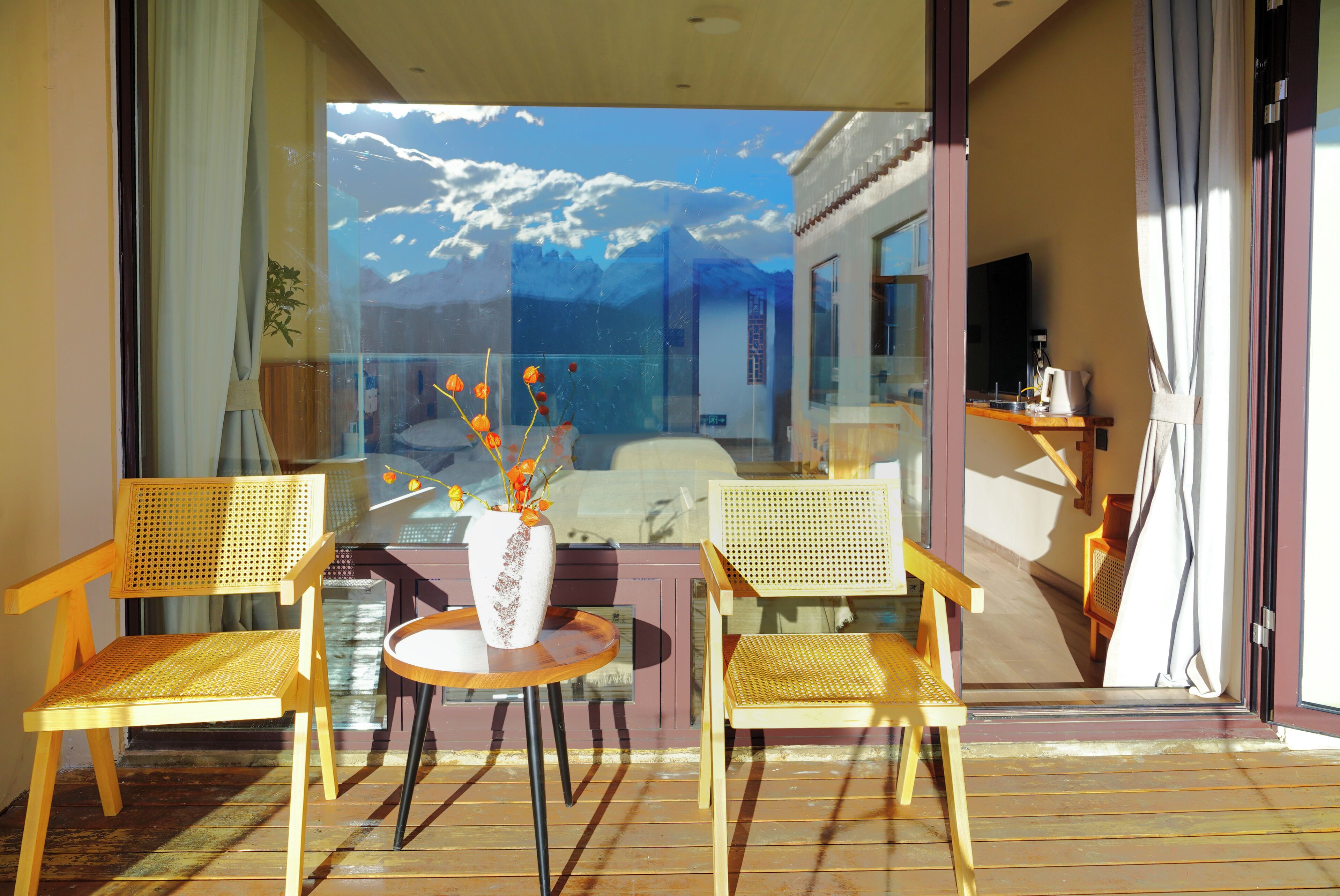 Ein Balkon mit zwei Holzstühlen, einem kleinen runden Tisch und einer Vase mit Blumen.