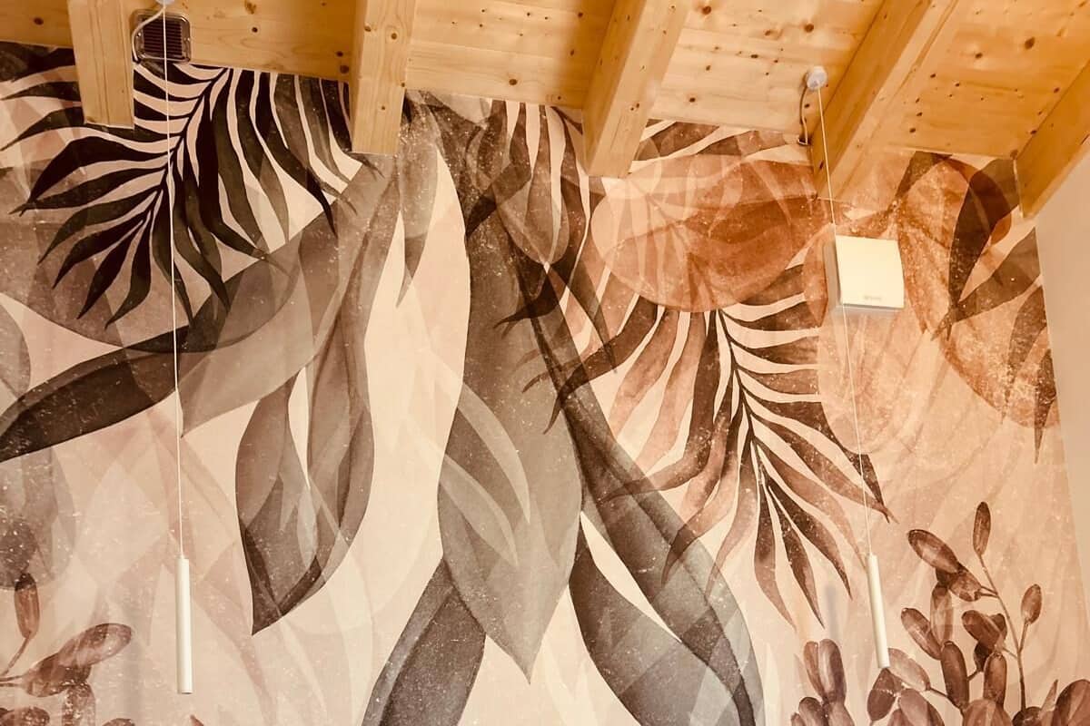 Habitación con dos camas, cada una con almohada blanca y colchón acolchado color beige. Las paredes están decoradas con un estampado grande y abstracto de hojas.