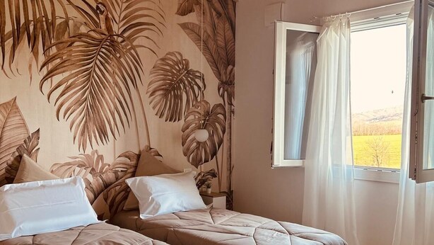 Een slaapkamer met twee bedden, een houten plafond en een groot raam met gordijnen.