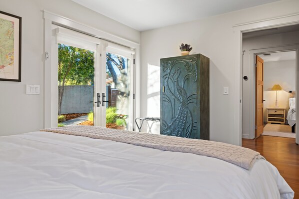 Een slaapkamer met een groot bed, een decor kast en uitzicht op de omgeving via een deur.