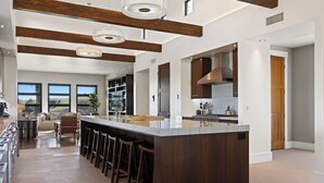 Une cuisine moderne dotée d’un grand îlot central, de tabourets de bar et offrant une vue sur l’extérieur.