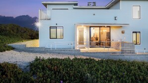 A modern two-story house with a balcony, large windows, and a well-lit interior. - Oceanfront 2BR + Rooftop Deck, & Beach Access | Strand Way B (Oceano)
