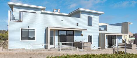 A modern two-story house with a balcony, large windows, and a concrete foundation.
