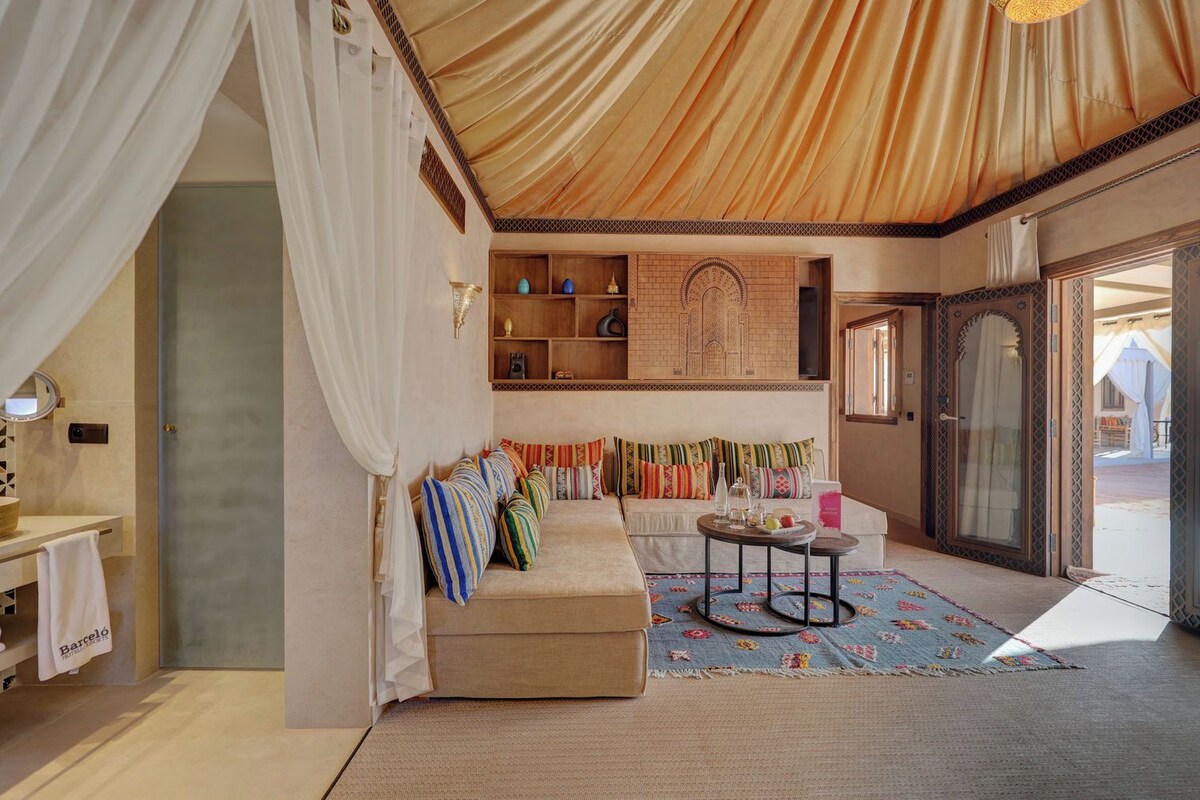 Quarto com sofá, uma mesa pequena, parede decorativa e porta que dá para o exterior.