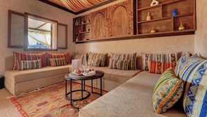 A cozy living room with a sofa set, a coffee table with fruits and a bottle, and a decorative wall with shelves. - Palmeraie Oasis Camp - A Member Of Barcelo Hotel Group (Marrakech)