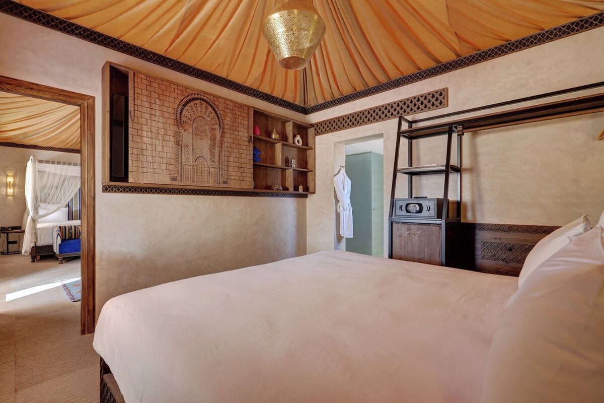 Un dormitorio con una cama grande, un armario, una tocador con espejo y una bata colgada.