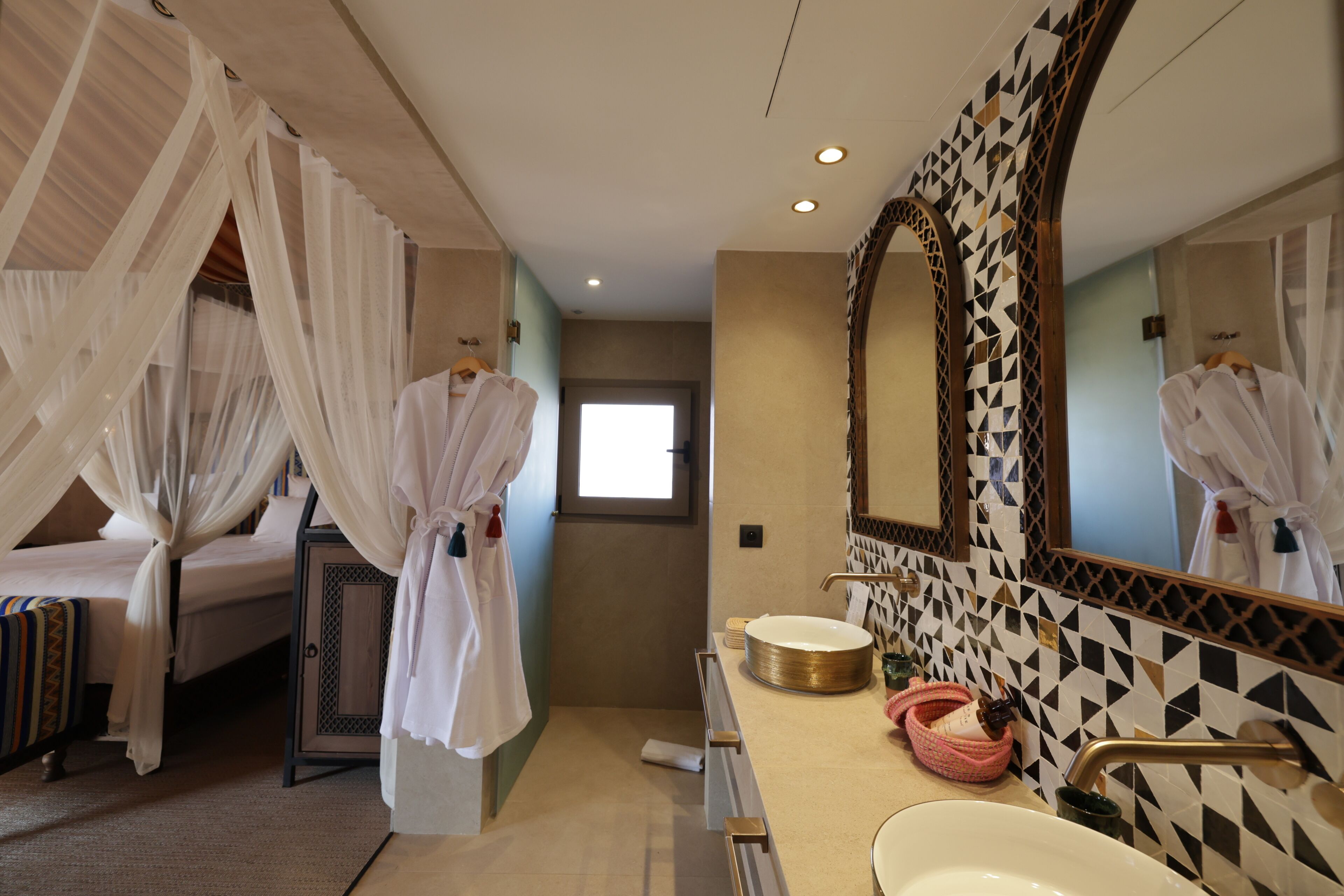 A hotel room with a bed, a bathroom with a large mirror, and a sink.