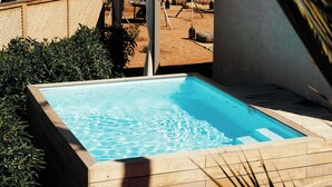 Un área de piscina con una piscina azul cristalina, rodeada de palmeras y un paisaje arenoso.
