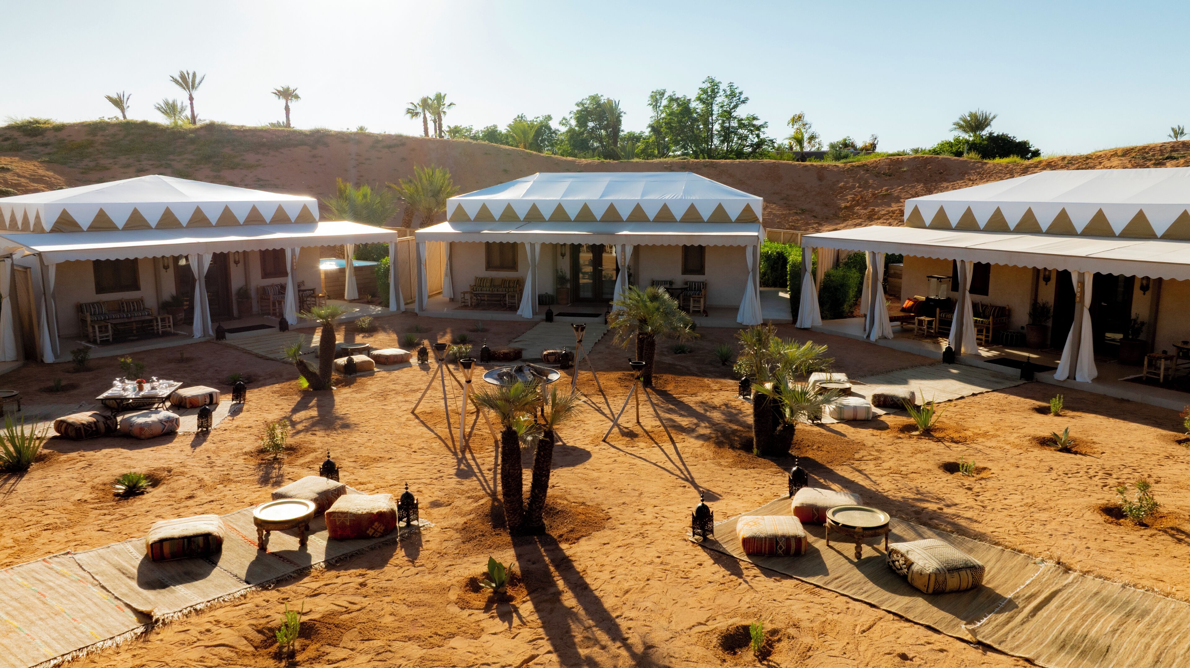 A desert resort with multiple tents, outdoor seating, and palm trees.