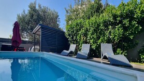 Ein Schwimmbecken mit Liegestühlen und einer überdachten Liegefläche.