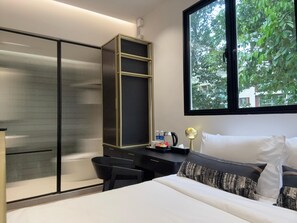 A modern hotel room with a bed, a desk, and a wardrobe. There is a window with a view of trees and buildings outside. - SOCIAL on Outram (Singapore)
