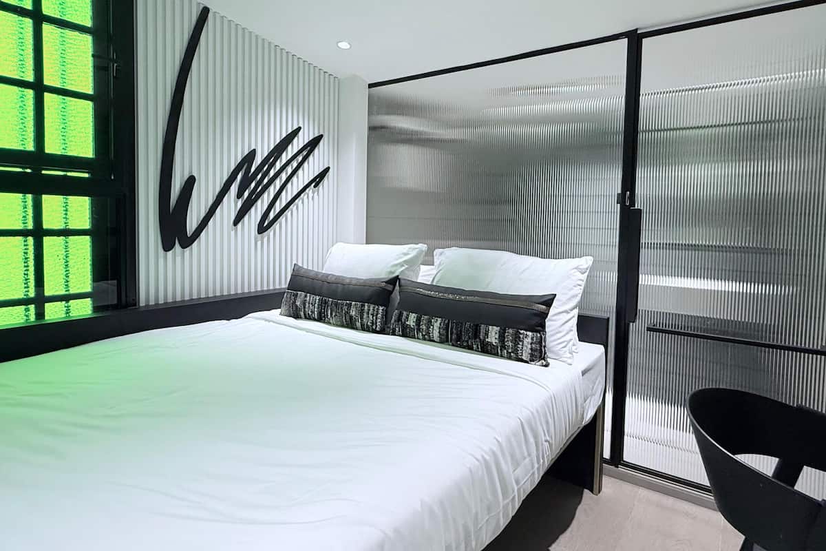 A modern bedroom with a large bed, a black chair, and a unique wall design.