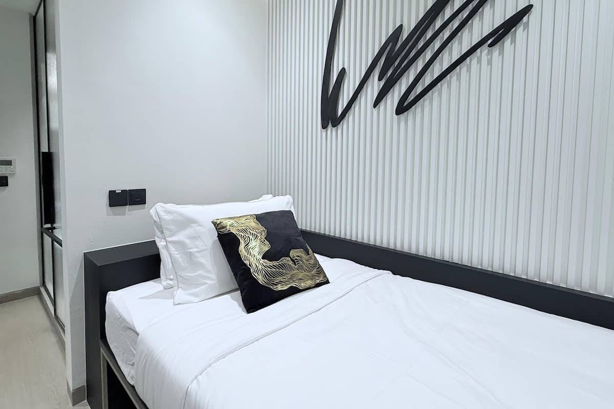 A modern bedroom with a black bed frame, white bedding, and a decorative wall panel.