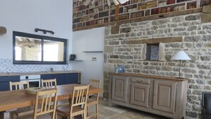 A kitchen with a stone wall, wooden cabinets, and a dining table with chairs. - Gîte Le Catalpa- vacation home (Normier)