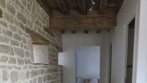 A stone wall with a wooden bench, a tiled floor, and a hallway leading to a room with two chairs. - Gîte Le Catalpa- vacation home (Normier)