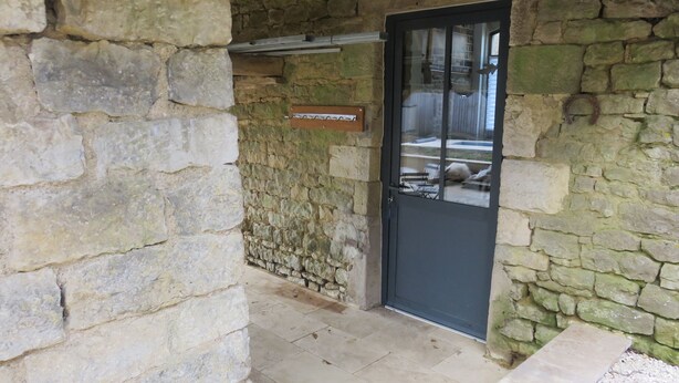 A stone-walled entrance with a black door, a sign above the door, and a tiled floor. - Gîte Le Catalpa- vacation home (Normier)