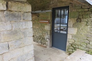 Una entrada de paredes de piedra con una puerta negra, un cartel sobre la puerta y un piso de baldosas.