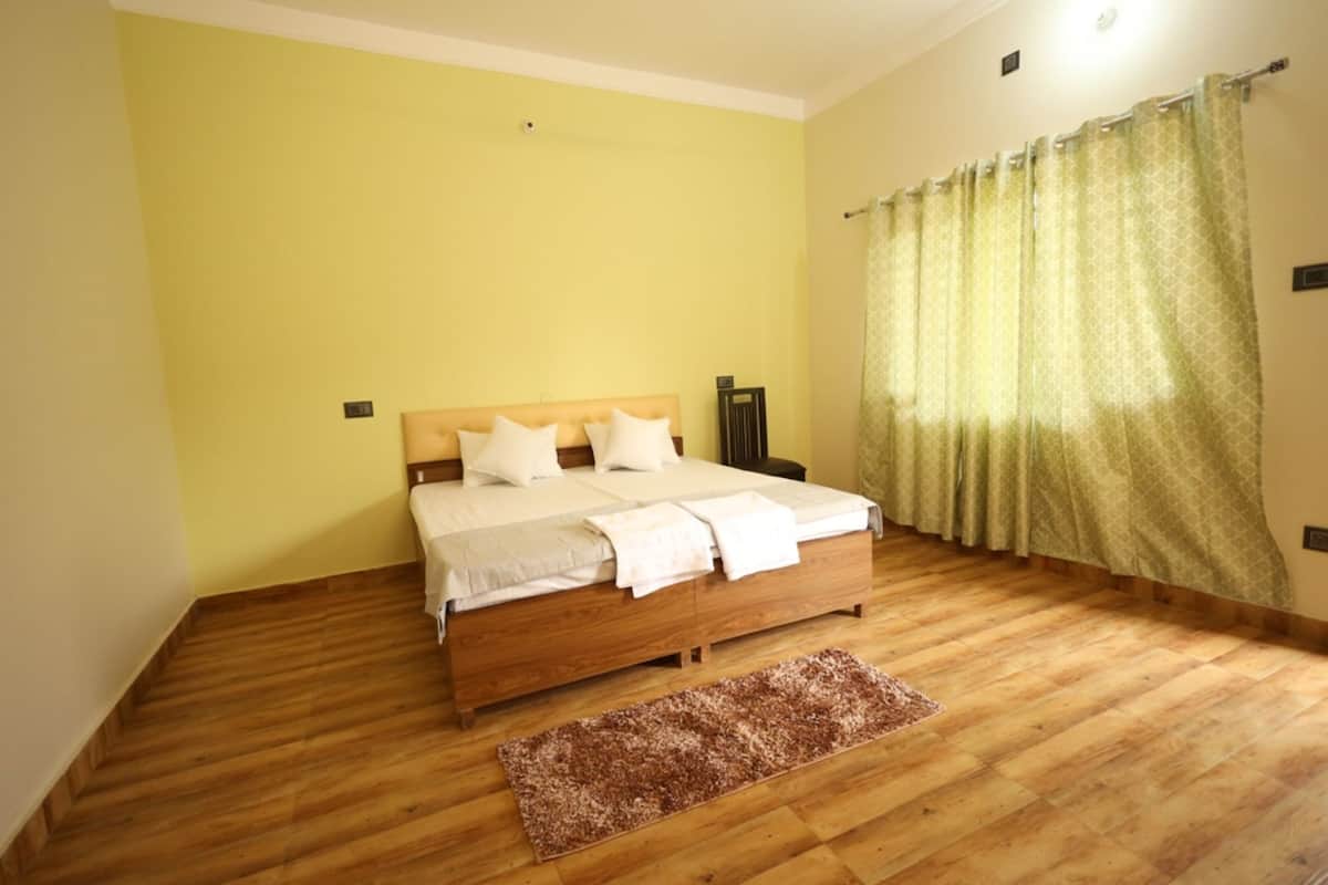 Une chambre avec un lit en bois, une tête de lit, une table de chevet, une chaise, un rideau à motifs et un plancher en bois.