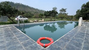 An outdoor swimming pool with a lifebuoy, surrounded by a tiled deck and natural scenery. - Kattapathar Nature Resort (Vikasnagar)