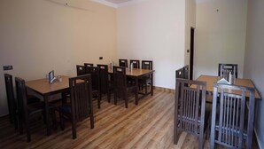 A dining area with a wooden table and chairs, a ceiling fan, and a door in the background. - Kattapathar Nature Resort (Vikasnagar)