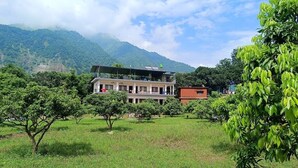 A building with multiple floors, surrounded by lush greenery and mountains in the background. - Kattapathar Nature Resort (Vikasnagar)