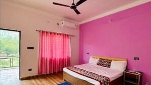 A bedroom with a wooden bed, a ceiling fan, a pink wall, and a view of greenery outside. - Kattapathar Nature Resort (Vikasnagar)