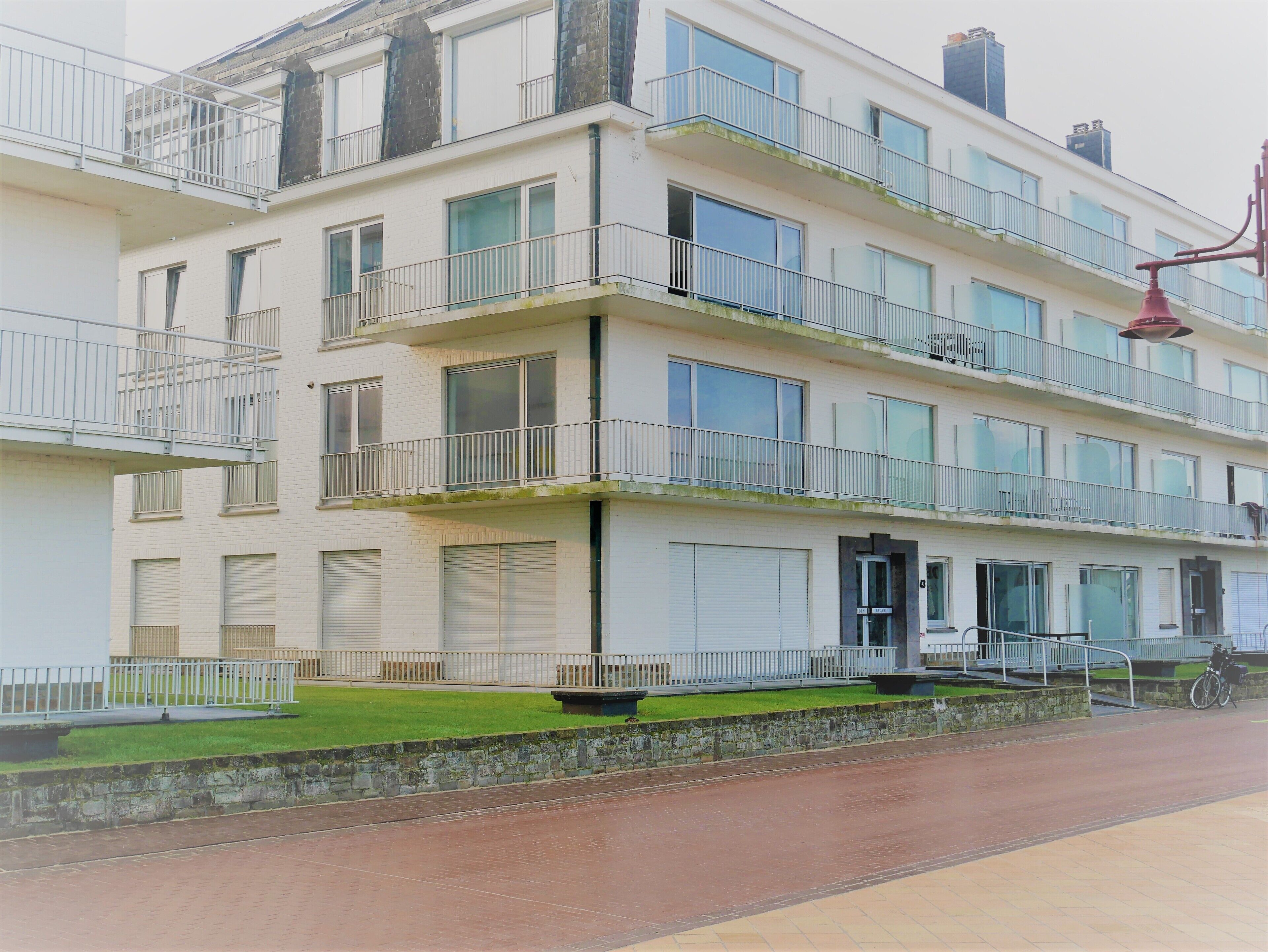 A multi-story residential building with balconies, large windows, and a paved walkway.
