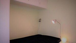 A small room with a single bed, a nightstand with a lamp, and a wall-mounted heater.