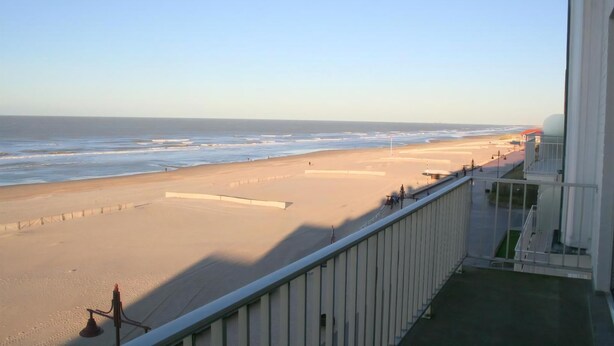 A beach view from a balcony with a railing, a clear sky, and the ocean.