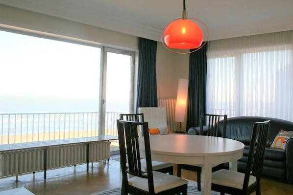 Une pièce avec une table ronde, des chaises, un canapé, une lampe et une vue sur la mer.