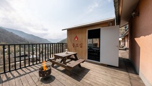 Una terraza de madera con un pozo de fuego, una mesa de picnic y un edificio de fachada de madera y una puerta.