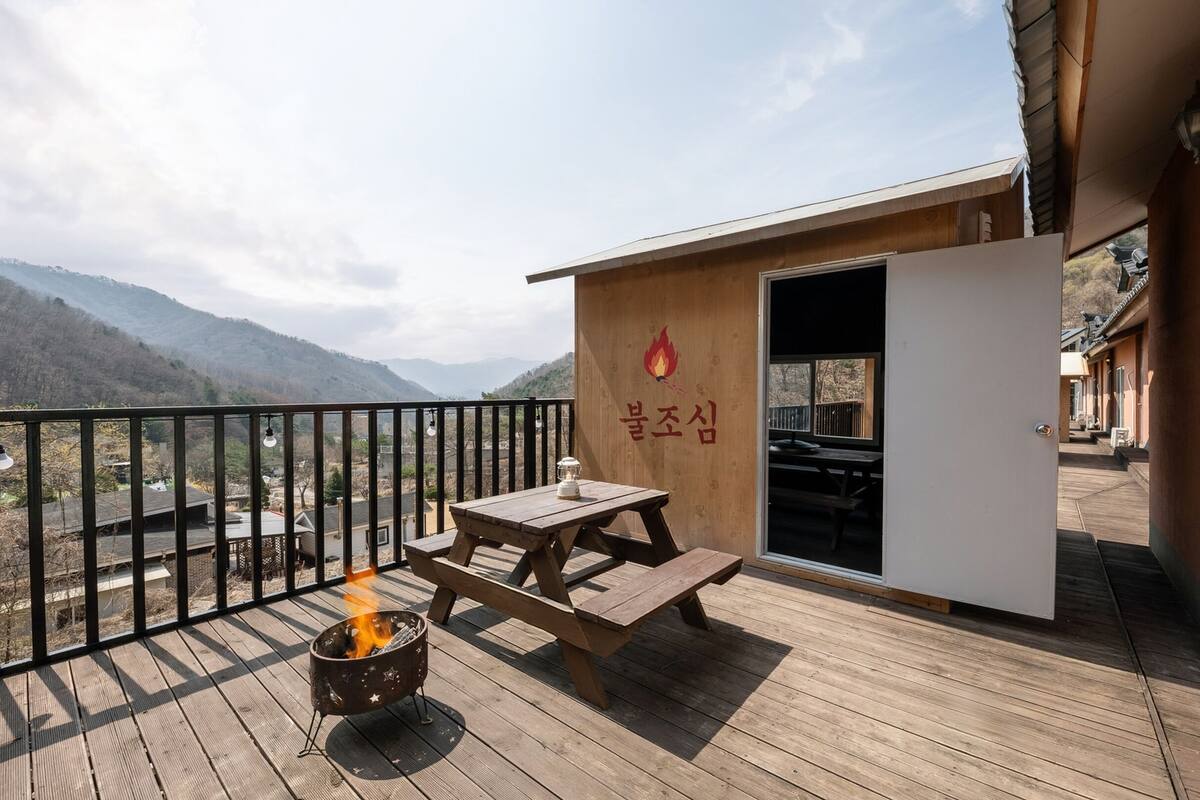 Una terraza de madera con un pozo de fuego, una mesa de picnic y un edificio de fachada de madera y una puerta.