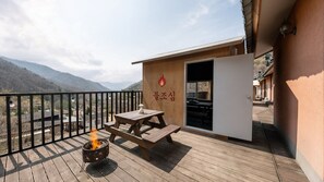 Una terraza de madera con un pozo de fuego, una mesa de picnic y un edificio de fachada de madera y una puerta.