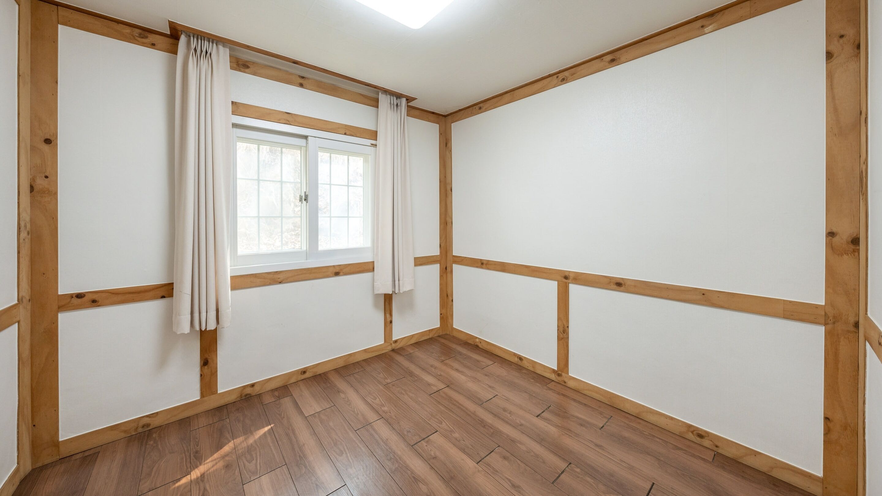 A room with wooden beams, a window with curtains, and a wooden floor.
