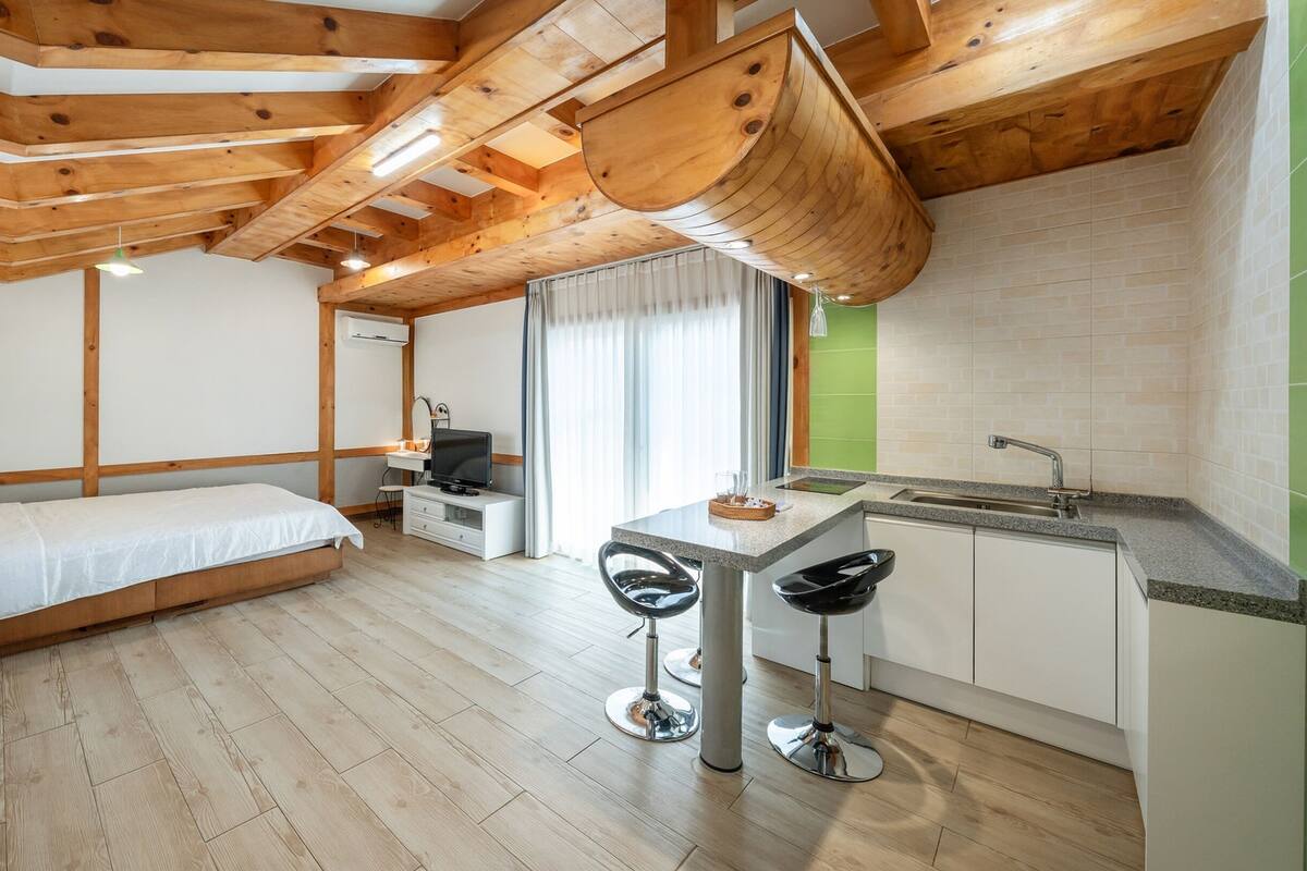 Una habitación compacta con cama, una kitchenette pequeña y una zona de comedor con taburetes.