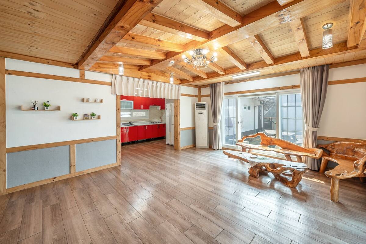 Amplia sala de estar con piso de madera, una cocina con armarios rojos y un ventanal con cortinas.
