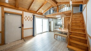 Una habitación amplia con una escalera de madera, un comedor y una cocina visible a través de una puerta abierta.