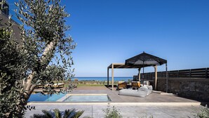 Een zwembadgedeelte met een pergola en zitplaatsen, met uitzicht op een heldere blauwe lucht en zee.