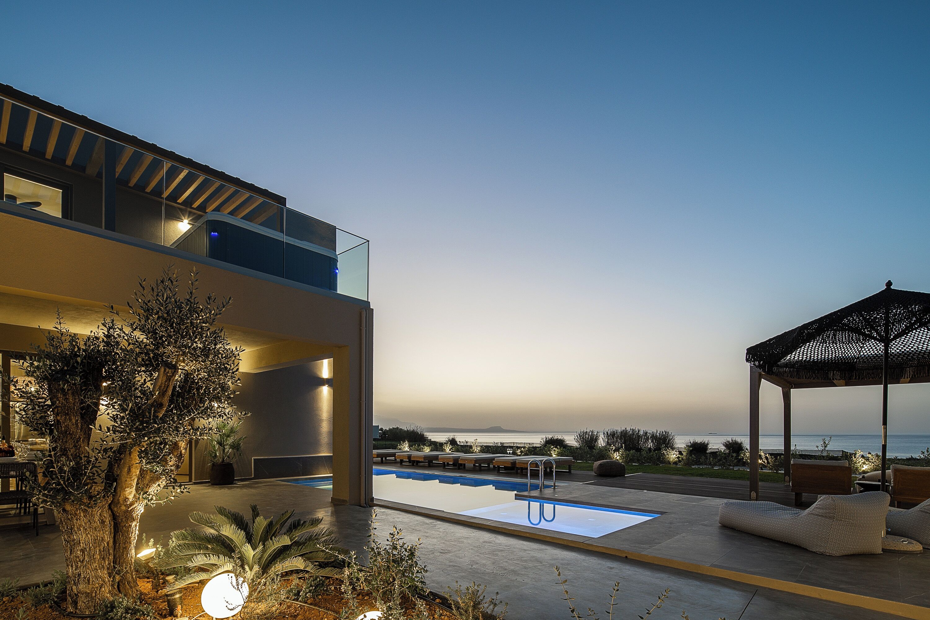 Ein moderner Poolbereich mit freiem Blick auf das Meer, einem überdachten Sitzbereich und einer Essgelegenheit.