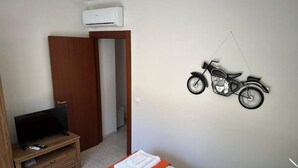 A hotel room with a bed, a TV on a wooden stand, an air conditioner, and a motorcycle wall decoration. - Andromeda  Rooms Otranto (Otranto)