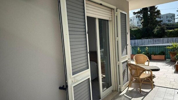 A balcony with sliding glass doors, wicker furniture, and a tiled floor. - Andromeda  Rooms Otranto (Otranto)