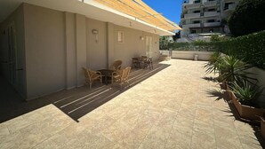 A covered outdoor area with a tiled floor, a small seating area with chairs and a table, and potted plants. - Andromeda  Rooms Otranto (Otranto)