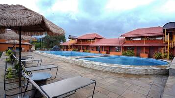 A resort with a swimming pool, outdoor seating, and thatched umbrellas.