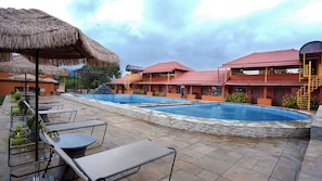 A resort with a swimming pool, outdoor seating, and thatched umbrellas.