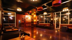A spacious indoor area with wooden flooring, tables, and chairs arranged for dining or socializing. - Map Resort (Alibag)