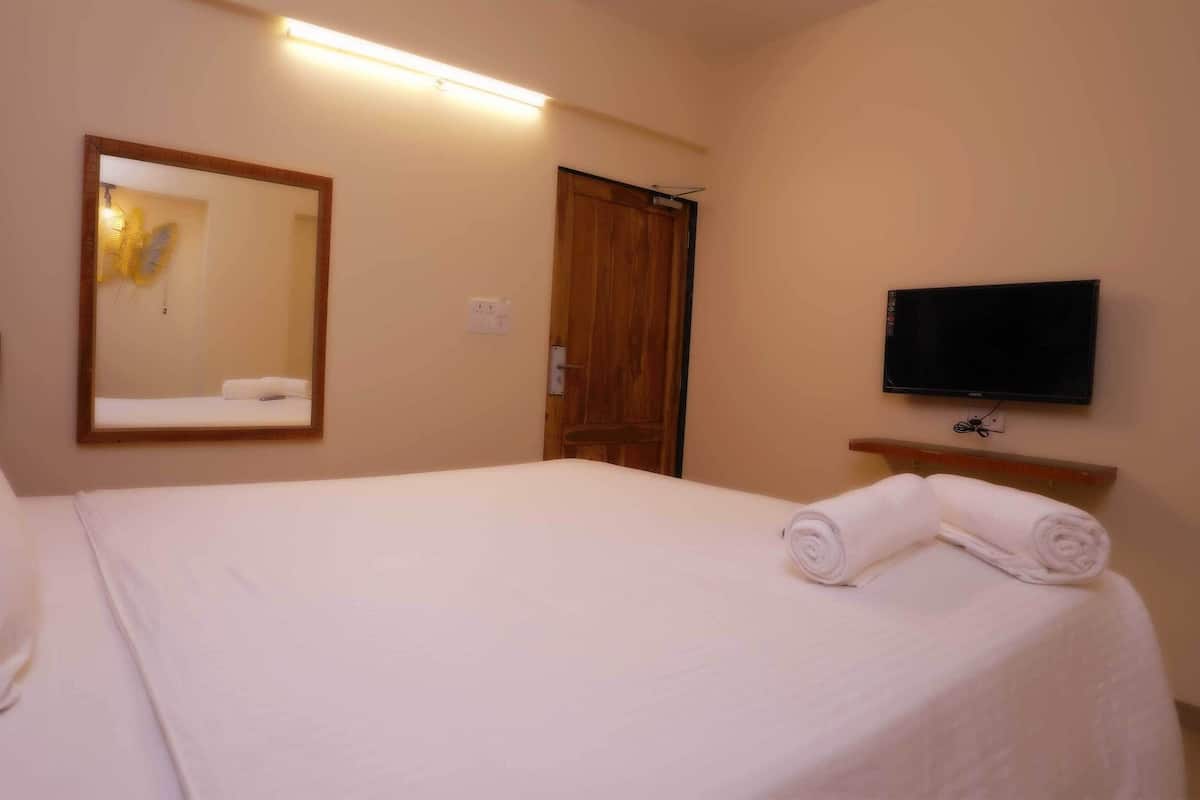 Quarto de hotel com cama, espelho, televisão e porta de madeira.