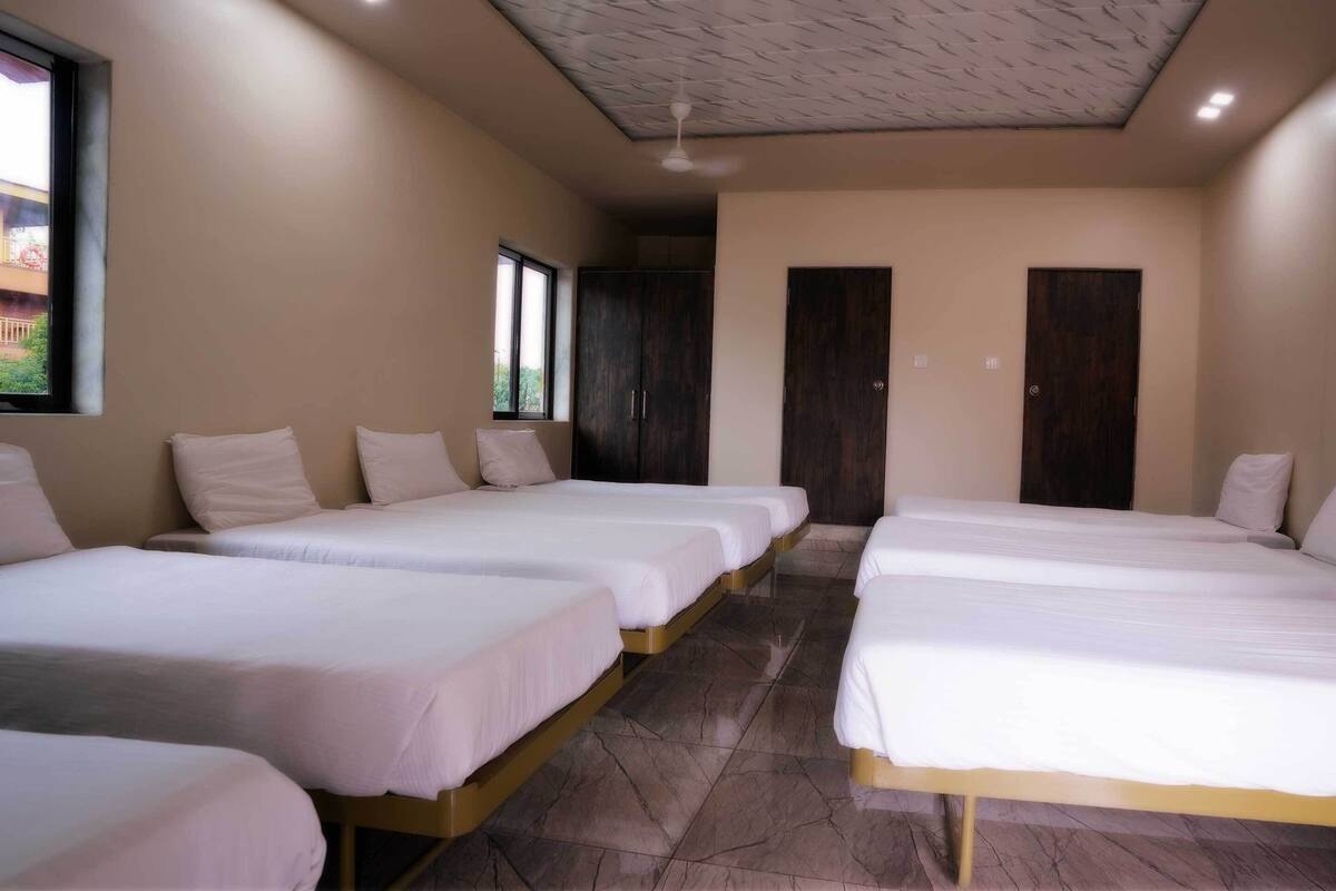 Quarto de hotel com quatro camas de solteiro, um ventilador de teto e uma janela grande.